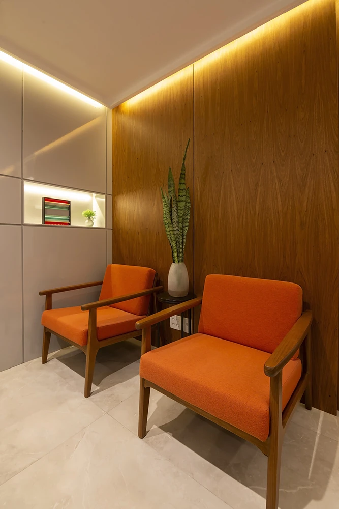 Uma sala elegante, clara e aconchegante, com luz embutida e cadeiras macias de cor laranja.